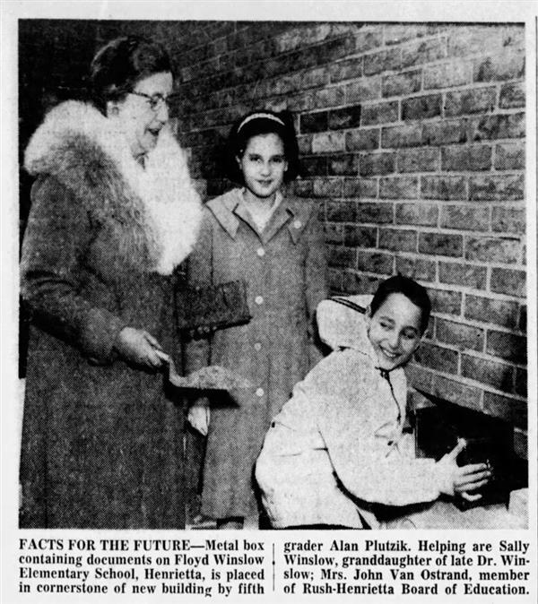 An adult and two students place a time capsule in the cornerstone of Winslow Elementary School.